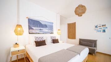 Une chambre à coucher avec un grand lit, deux tables de chevet, une lampe fixée au mur, une décoration murale en tissu tissé et un tableau encadré.