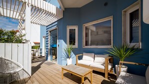 A wooden deck with a white sofa, a wooden table, and potted plants.