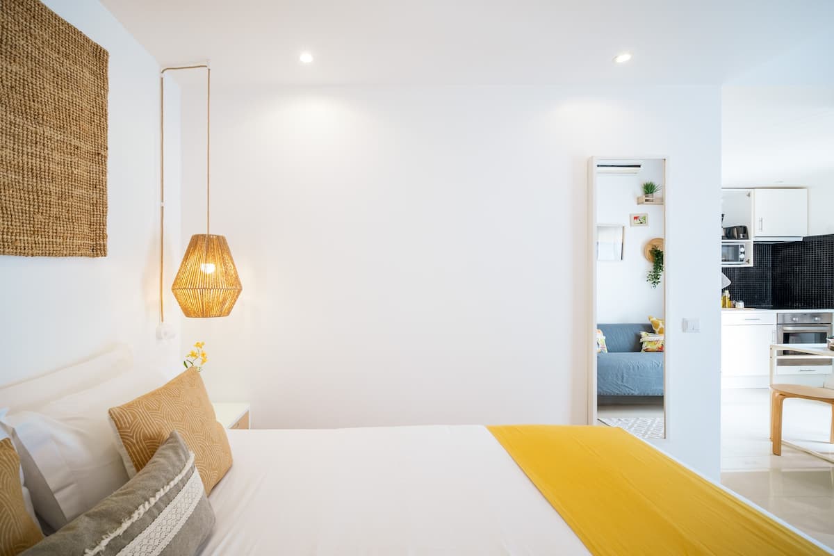 Een moderne slaapkamer met een groot bed, een bedlamp en uitzicht op de keuken.