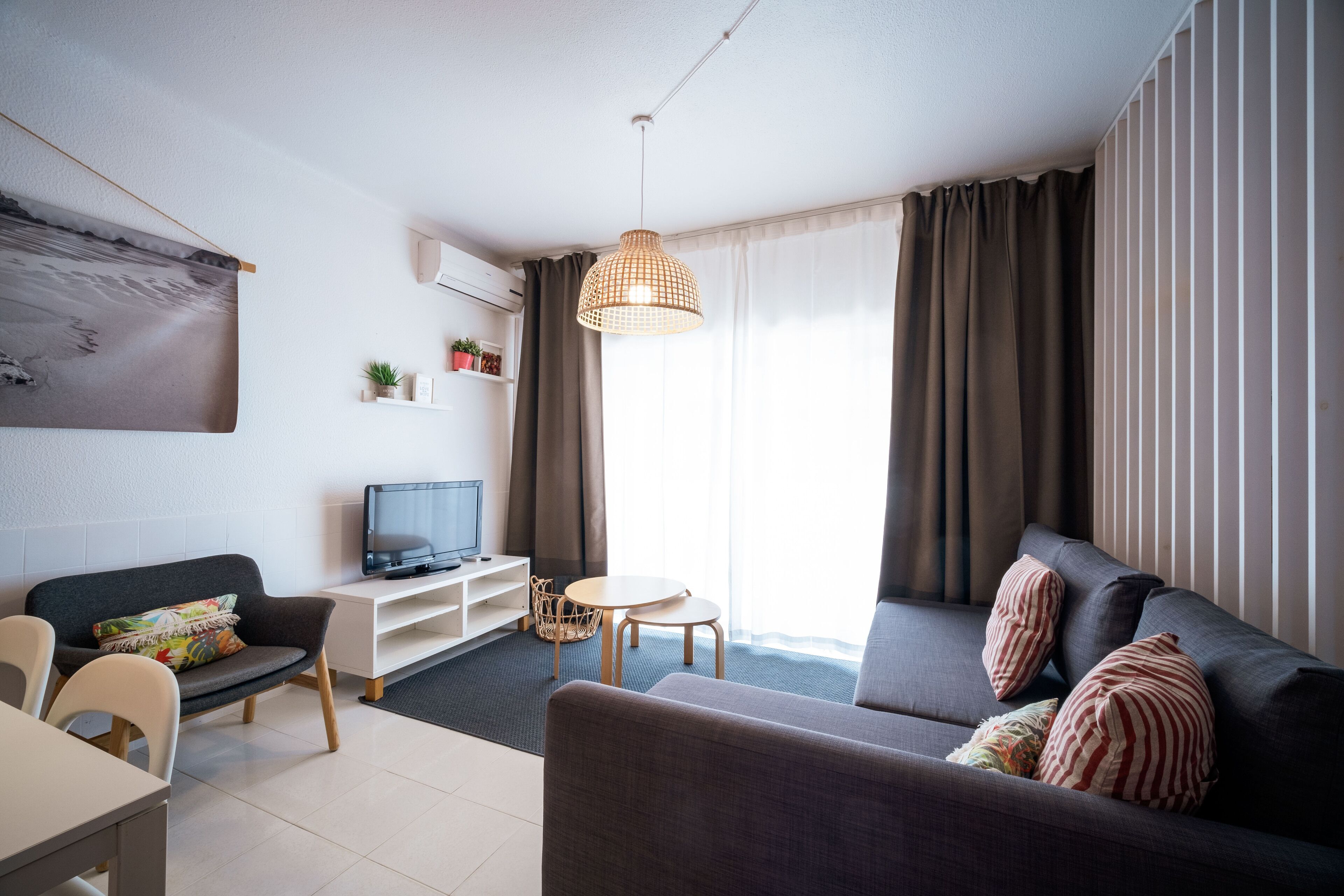 Una sala de estar moderna con un sofá, un televisor, una mesita y una lámpara colgante.