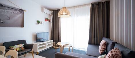 Una sala de estar moderna con un sofá, un televisor, una mesita y una lámpara colgante.