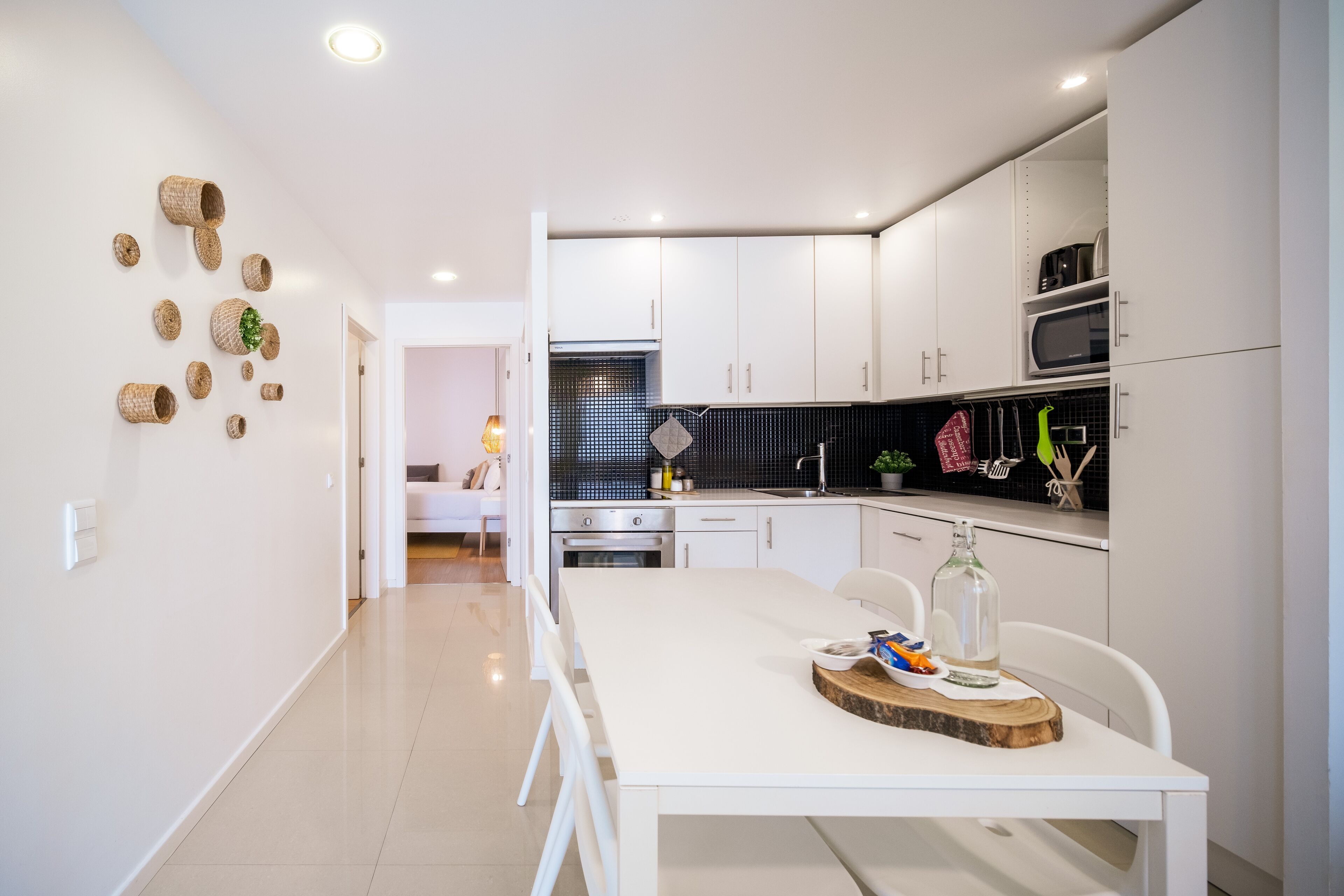 A modern kitchen with white cabinets, a black backsplash, and a dining area with a white table and chairs.