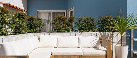 A modern outdoor seating area with a wooden sofa and a table, surrounded by potted plants and a blue wall.