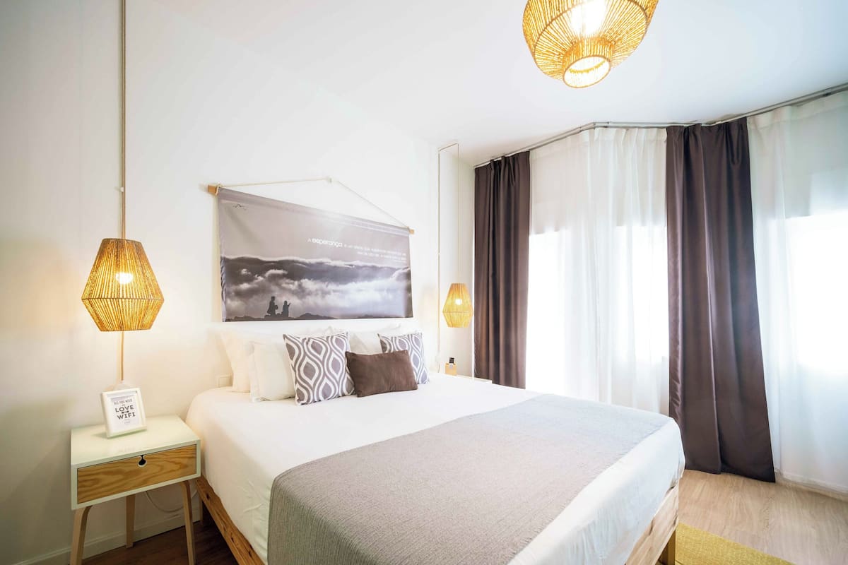 Een netjes ingerichte hotelkamer met een groot bed, een bedlampje, een ingelijste foto aan de muur en een raam met gordijnen.