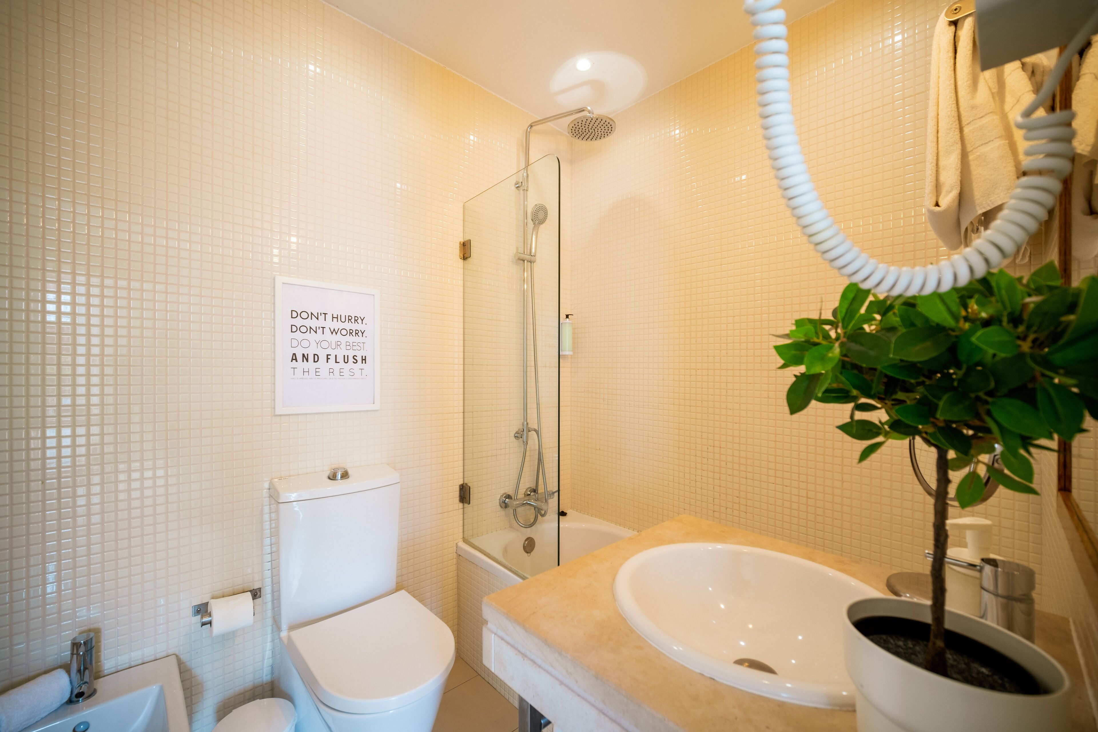 Ein Badezimmer mit Toilette, Waschbecken und Dusche. An der Wand befindet sich ein Schild und ein Blumentopf.
