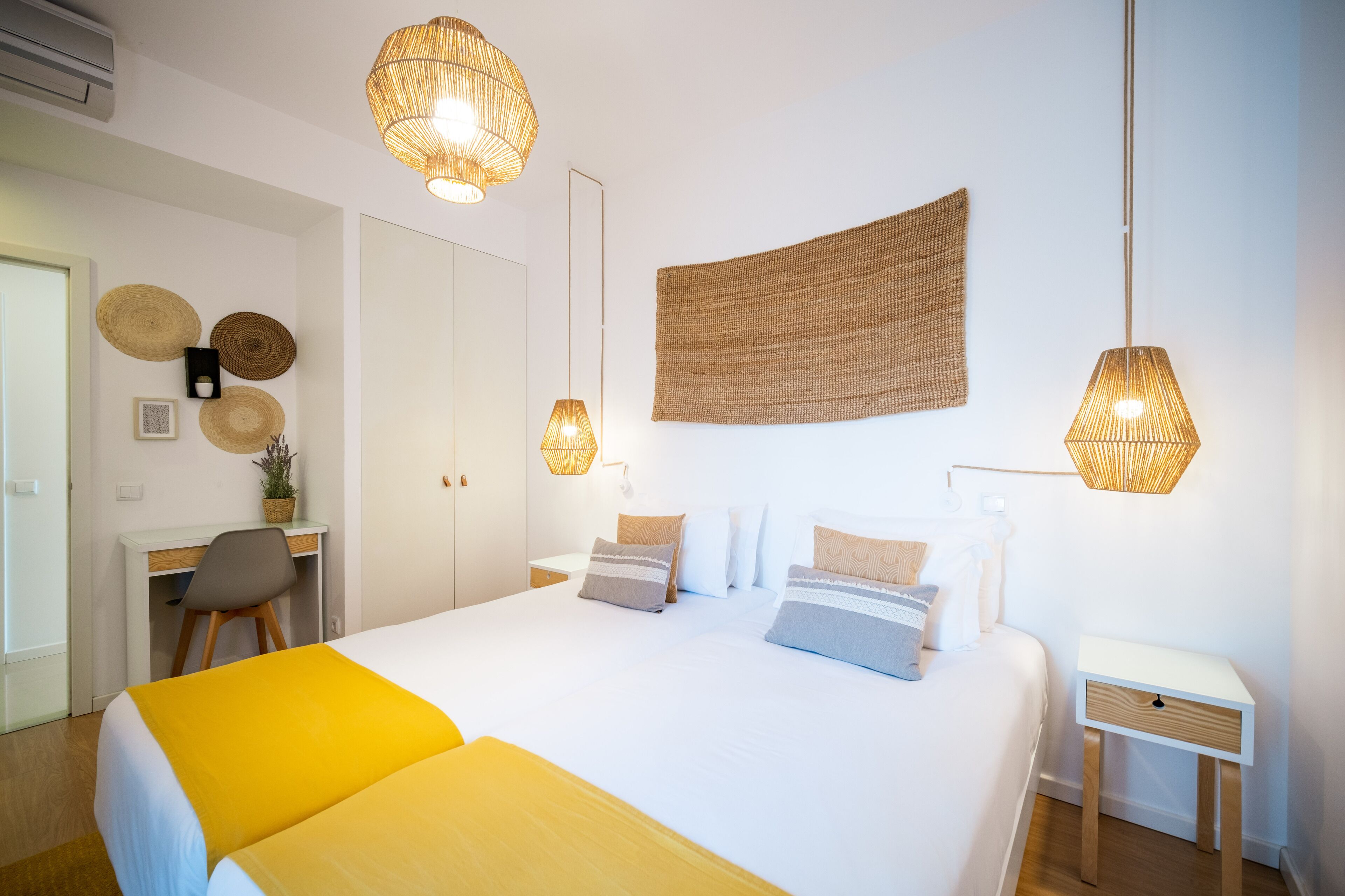 A modern bedroom with a large bed, bedside tables, a desk, and a hanging woven tapestry.