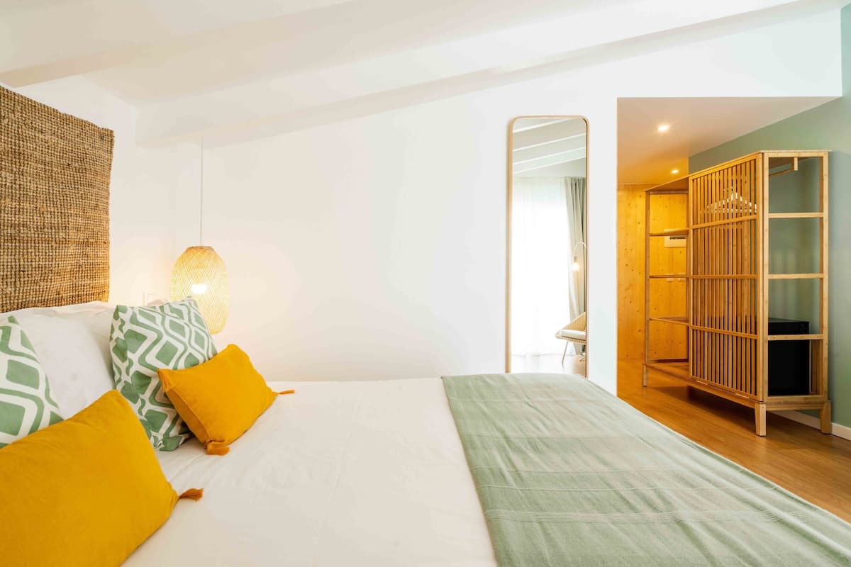 Een slaapkamer met een bed, kussens, een hanglamp en een houten garderobe.
