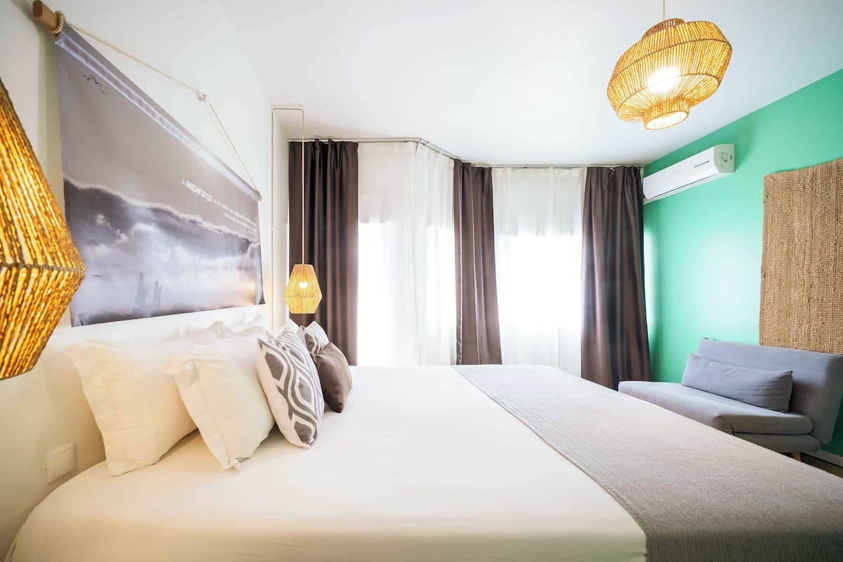 Een hotelkamer met een groot bed, een bank, een hanglamp en een wandairconditioner.