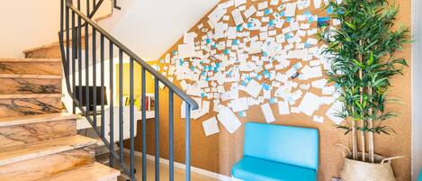 A staircase with a corkboard wall covered in notes, a blue bench, and a potted plant.