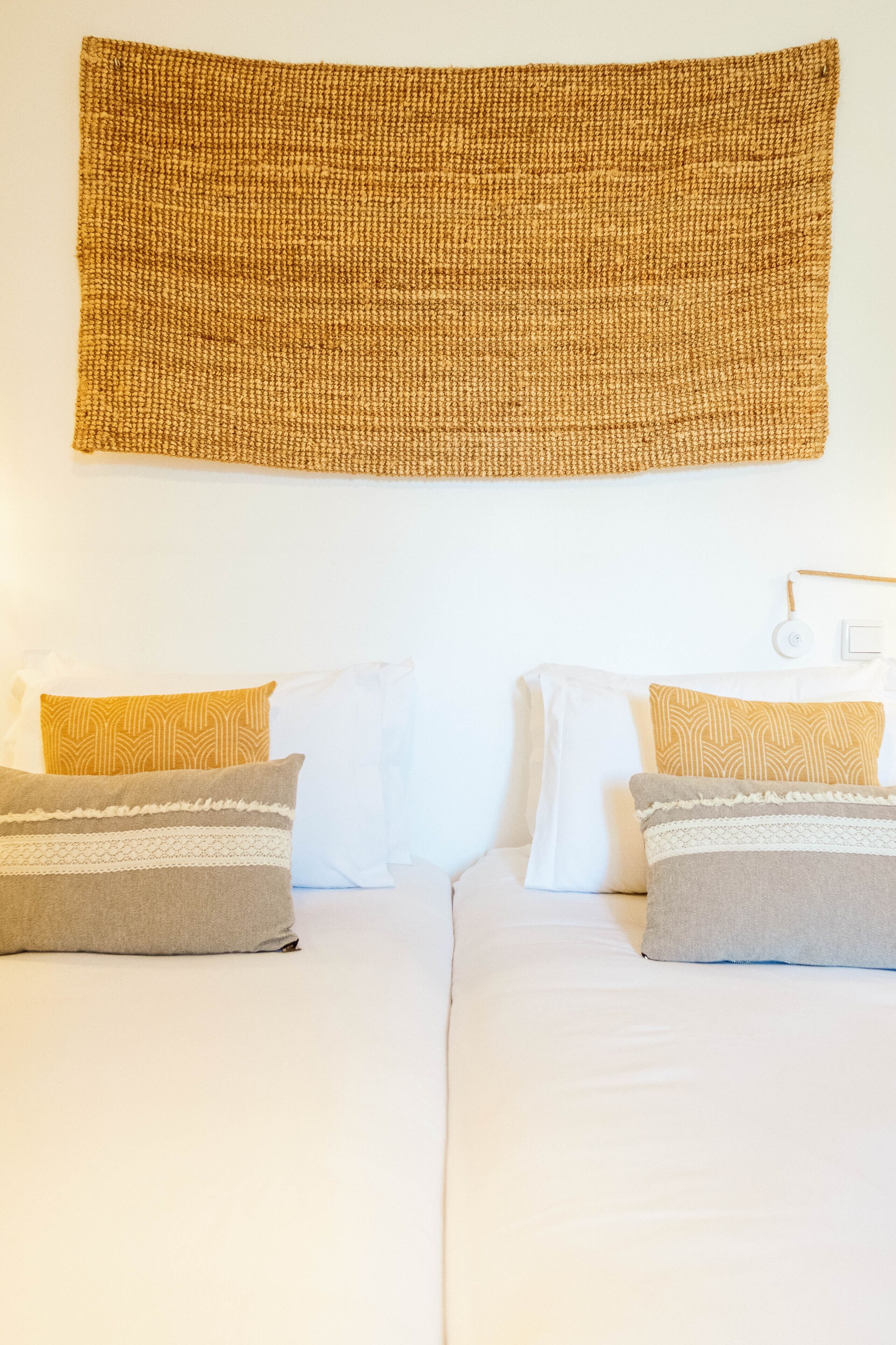 A double bed with white bedding and two pillows, one with a geometric pattern and the other plain.