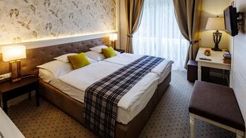Una habitación de hotel con una cama grande, dos mesitas de noche, un escritorio con lámpara, un televisor y una ventana con cortinas.
