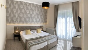 Een netjes ingerichte slaapkamer met een groot bed, een nachtkastje met een lamp, een klein bureau en een raam met gordijnen.