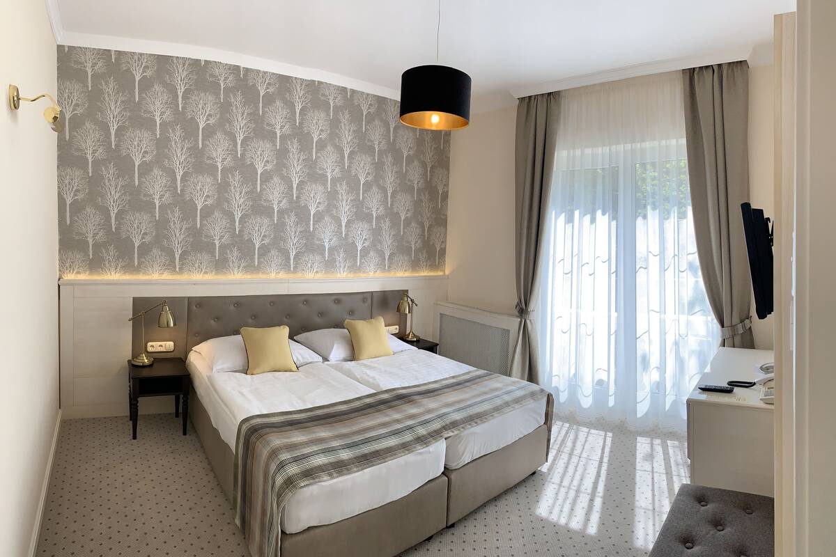 Une chambre à coucher bien rangée, avec un grand lit, une table de chevet avec une lampe, un petit bureau et une fenêtre avec des rideaux.