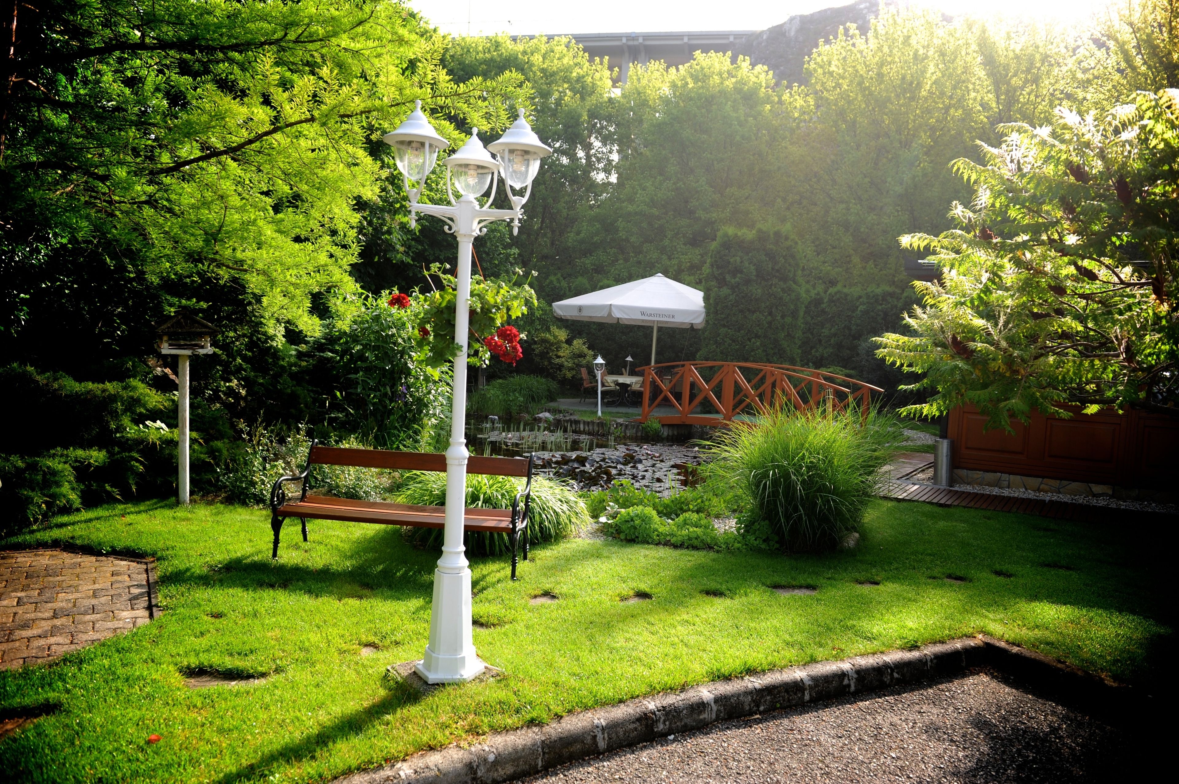 Un jardín con un banco, un farol y un pequeño puente.