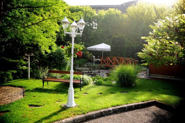 A garden with a bench, a lamp post, and a small bridge.