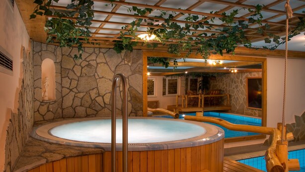 Een hottubgedeelte met houten vloeren, stenen muren en een pergola met hangende wijnranken.