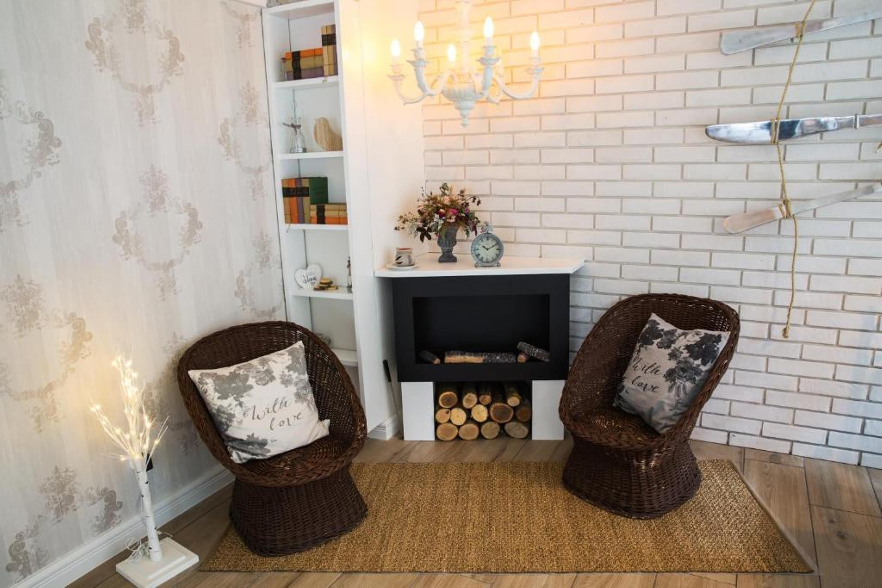 A cozy room with a fireplace, two wicker chairs with cushions, a small shelf with books and decorative items, and a wall-mounted knife rack.