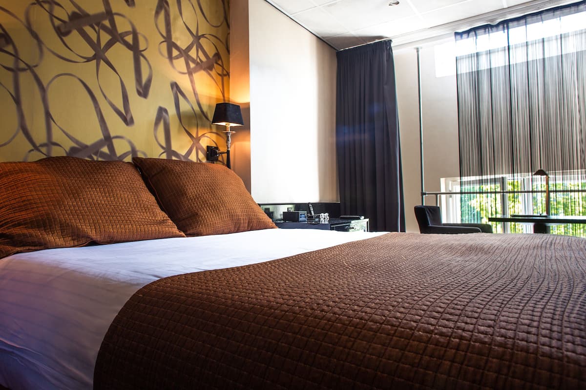 A hotel room with a large bed, a desk, a chair, and a window with curtains.