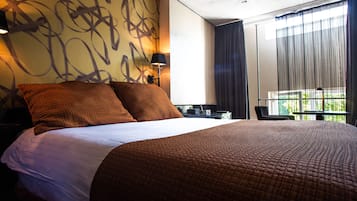 Una habitación de hotel con una cama grande, un escritorio, una silla y una ventana con cortinas.