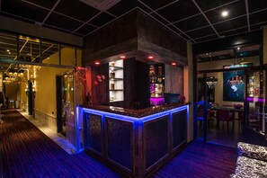 Una zona de bar con mostrador de madera, estantes con botellas y un área de descanso con un sofá estampado.