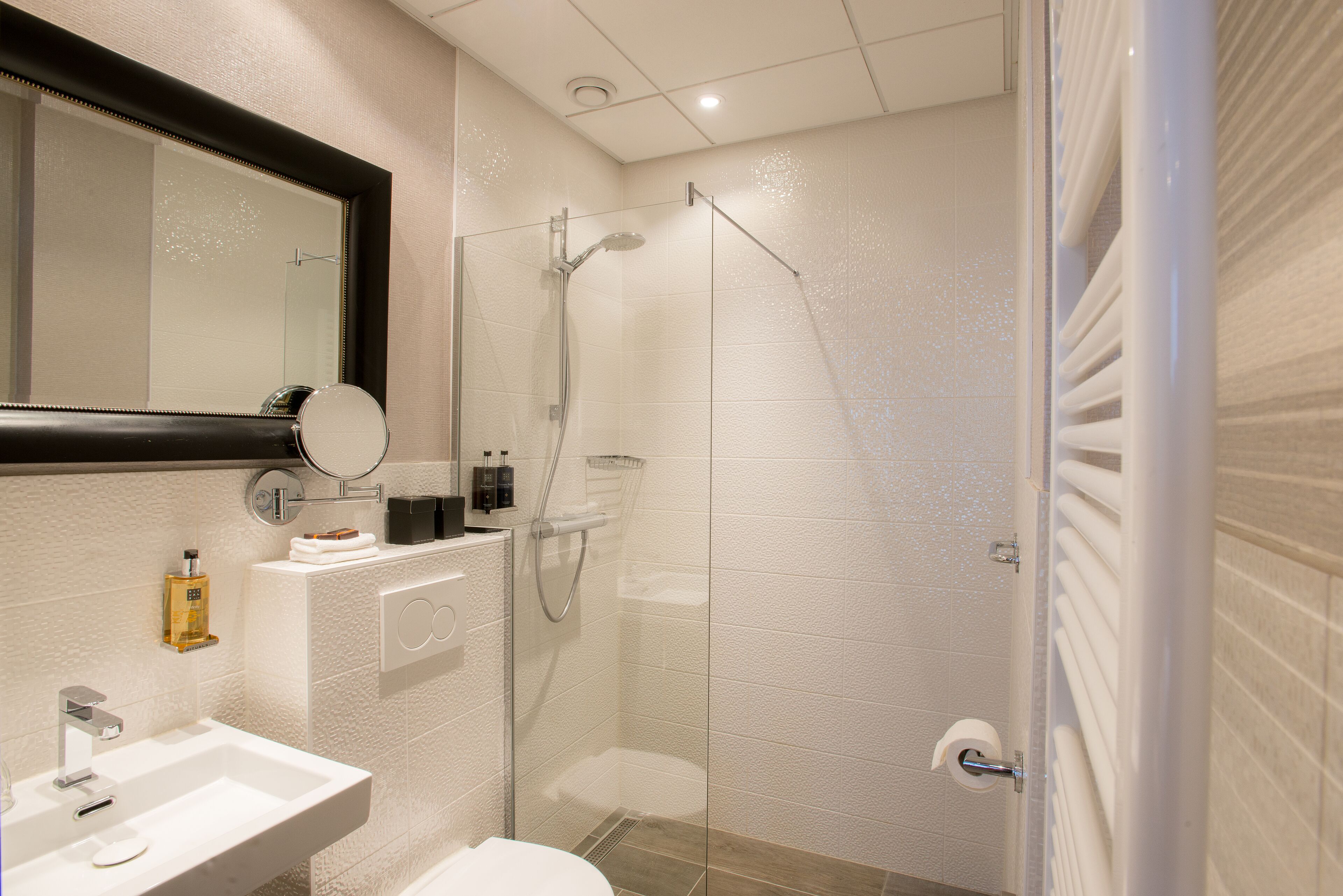 Une salle de bain moderne avec une douche à parois de verre, un lavabo blanc et un grand miroir.