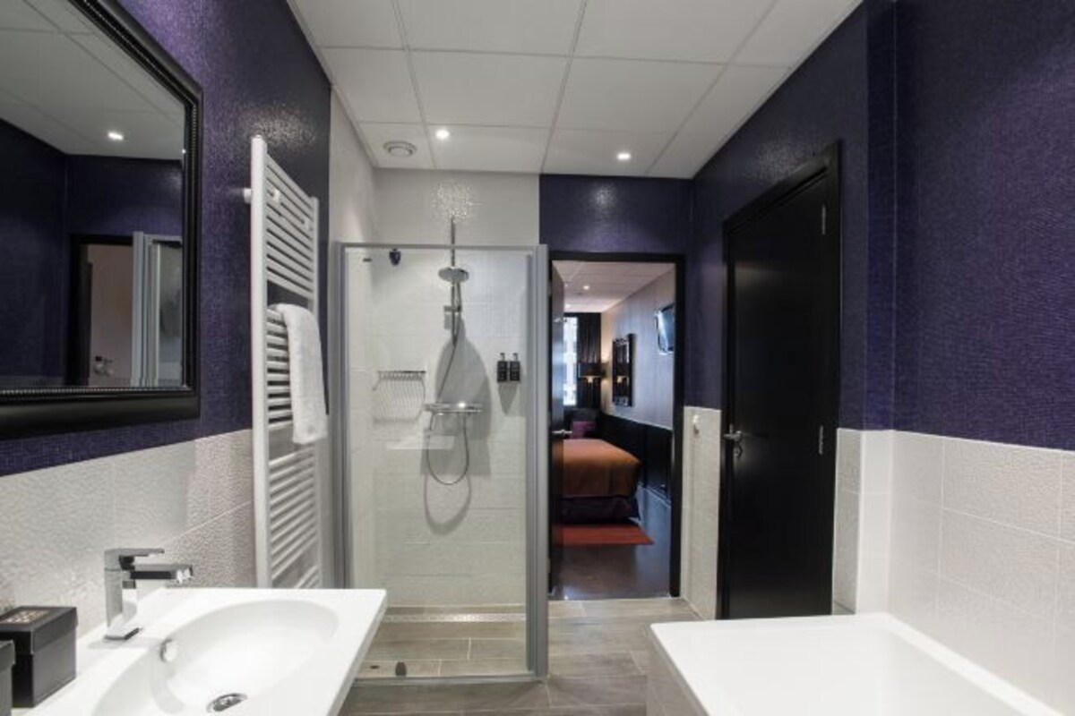 Un baño moderno con ducha de vidrio, lavamanos blanco y puerta negra.