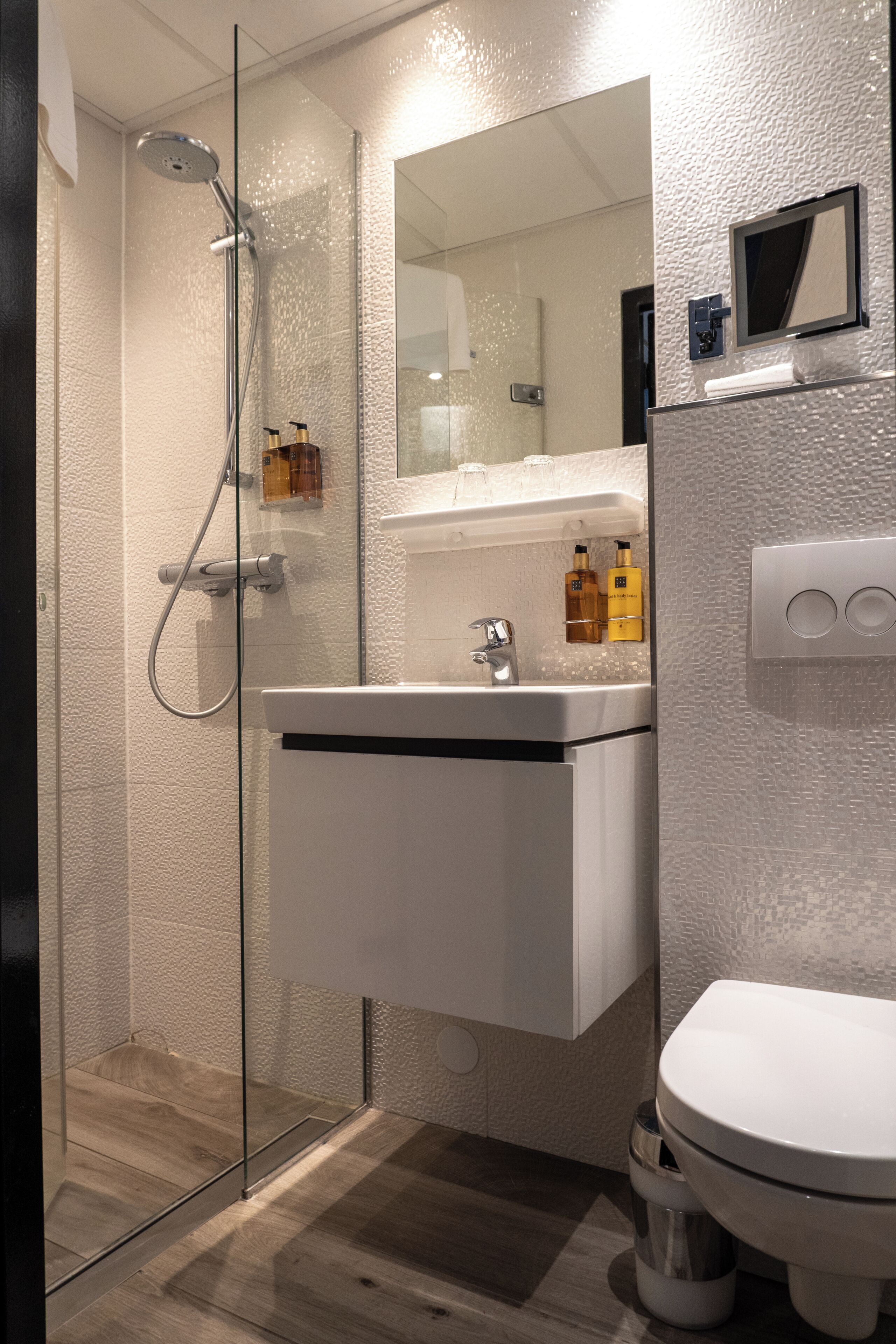A modern bathroom with a glass-enclosed shower, a white sink with a mirror above, and a toilet.