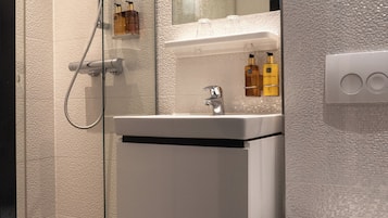 A modern bathroom with a glass-enclosed shower, a white sink with a mirror above, and a toilet.