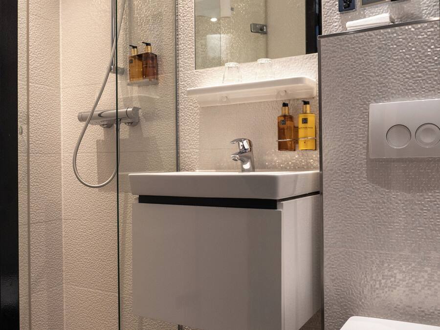 Une salle de bain moderne avec une douche à parois de verre, un lavabo blanc avec un miroir au-dessus et des toilettes.