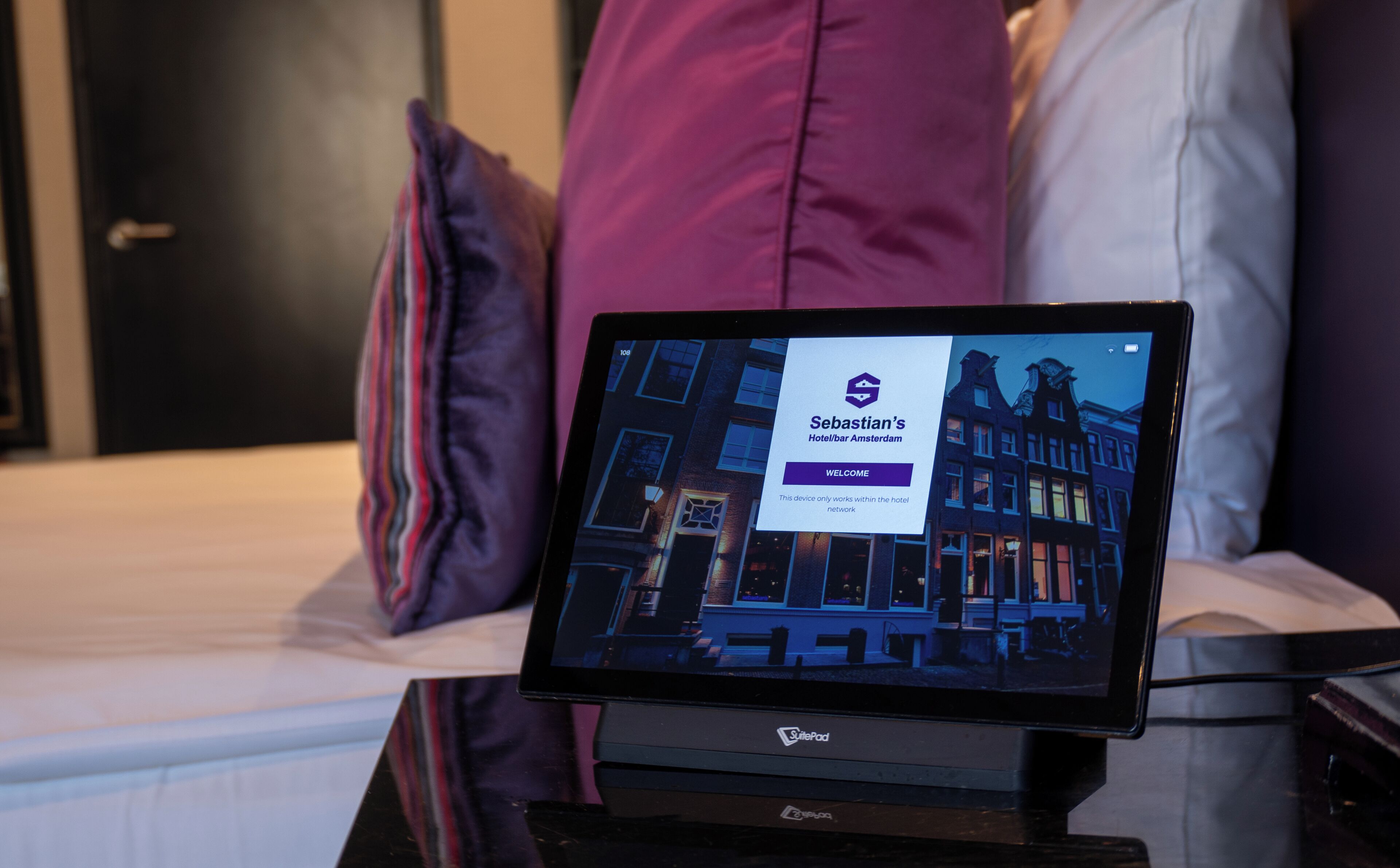 Una tableta mostrando la página web de un hotel sobre la mesita de noche en una habitación de hotel.