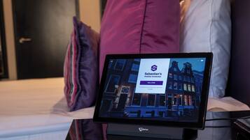Una tableta mostrando la página web de un hotel sobre la mesita de noche en una habitación de hotel.