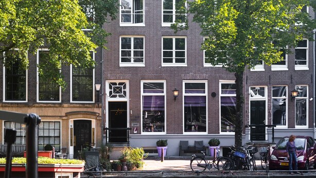 A canal-side building with a brick facade, large windows, and a small boat docked in front. - Hotel Sebastian's (Amsterdam)