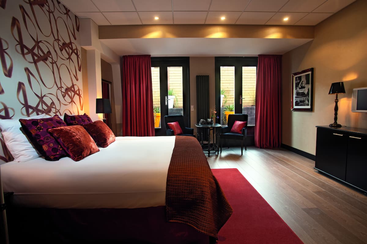 A hotel room with a large bed, a desk, two chairs, a TV, and a red carpet.