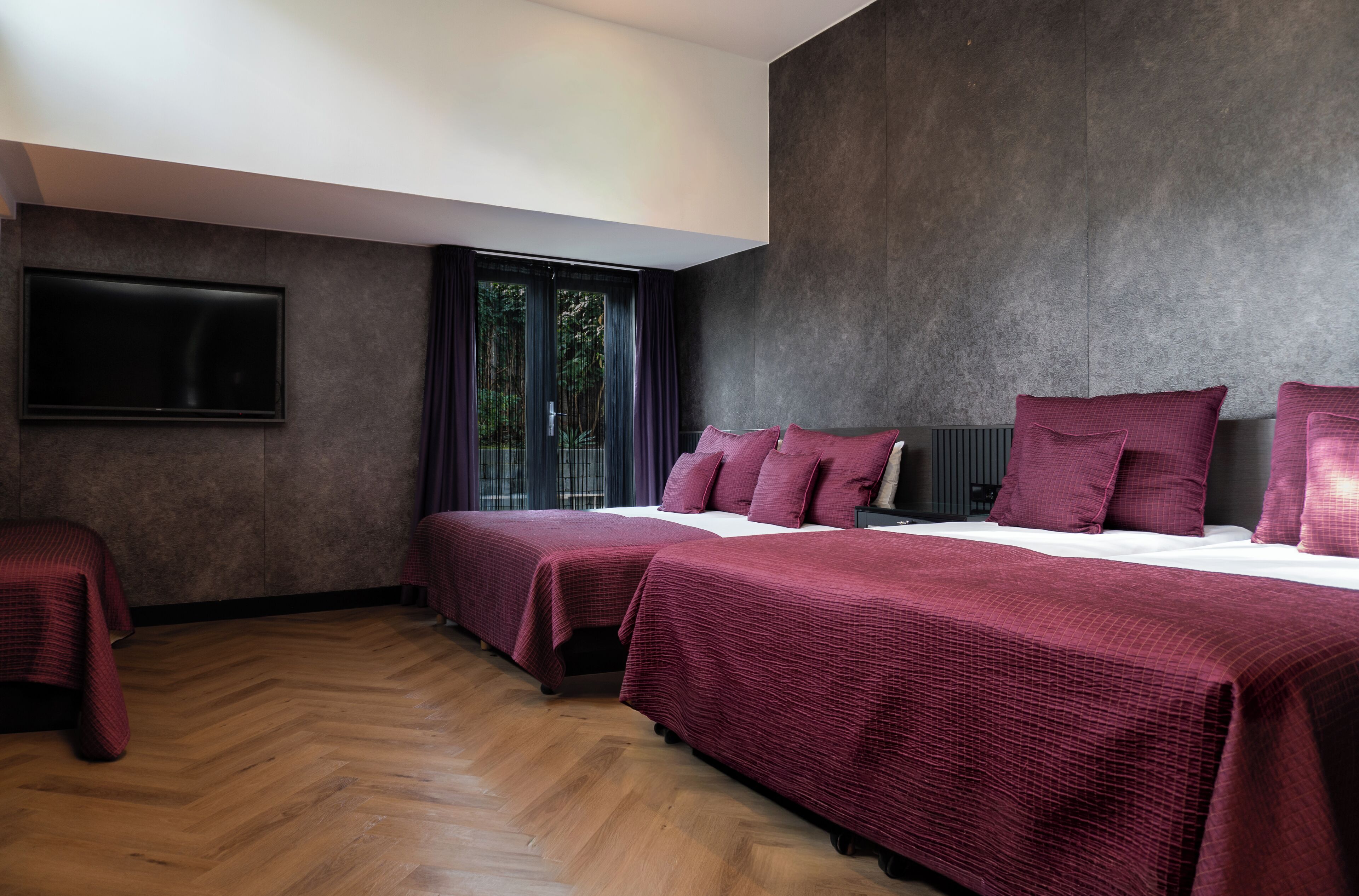 A hotel room with two beds, a flat-screen TV, and a large window with curtains.