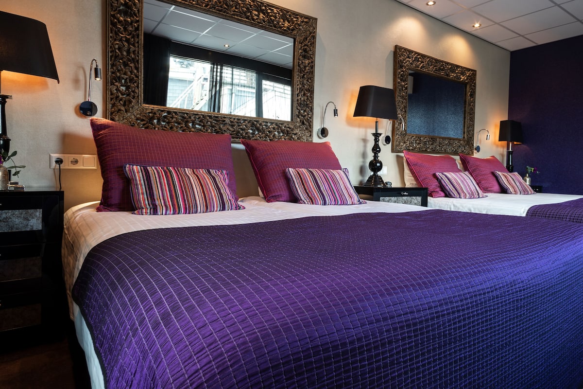A hotel room with two beds, purple bedding, and large mirrors.
