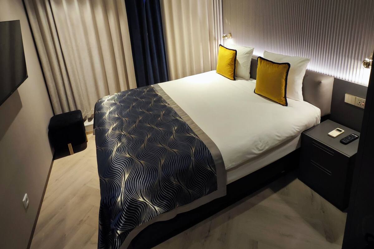 A modern hotel room with a large bed, bedside tables, a wall-mounted TV, and a ceiling vent.