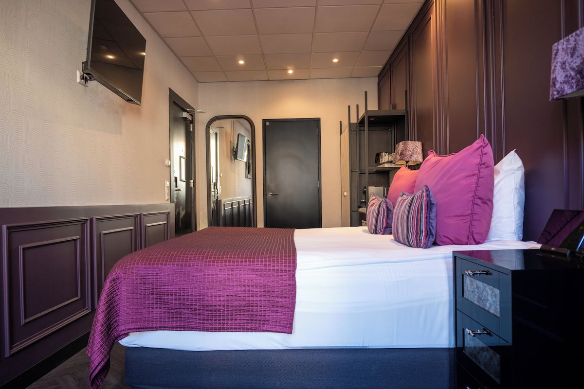A hotel room with a large bed, a bedside table, a wardrobe, and a mirror.