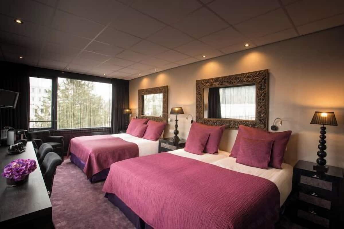 A hotel room with two beds, a desk, and a TV.