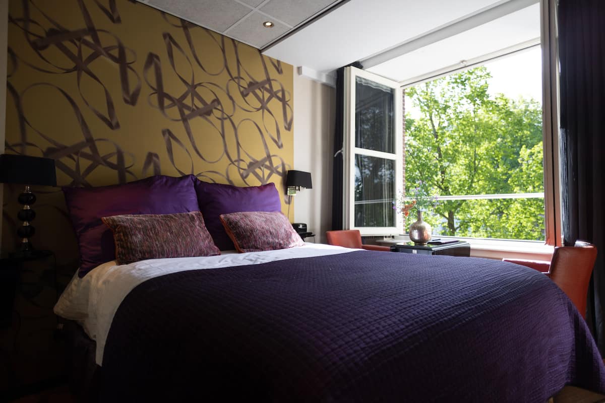 A hotel room with a large bed, a window with a view of trees, and a modern wall design.