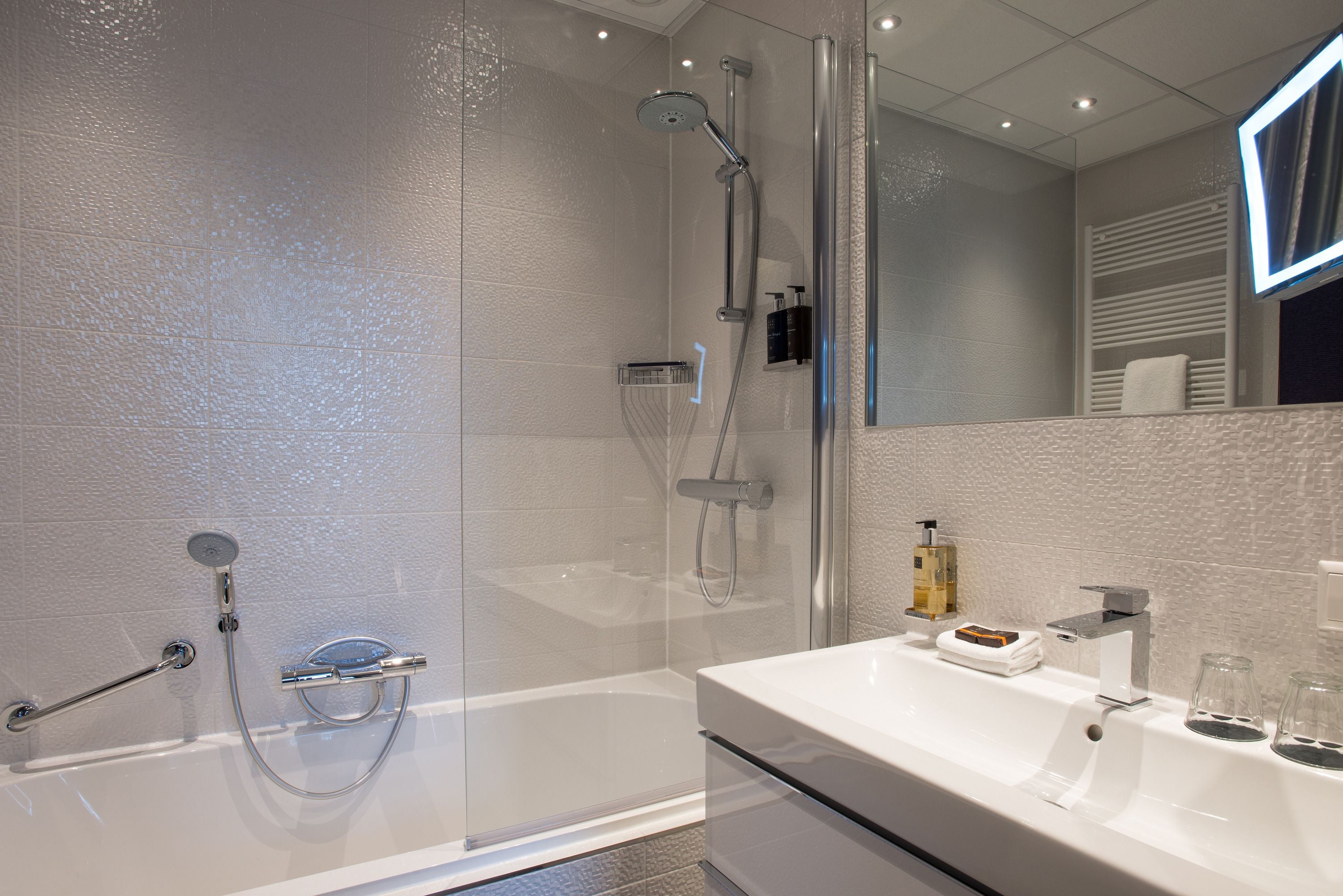 Une salle de bain moderne avec une douche à parois de verre, un lavabo blanc et un miroir doté d’un cadre éclairé.