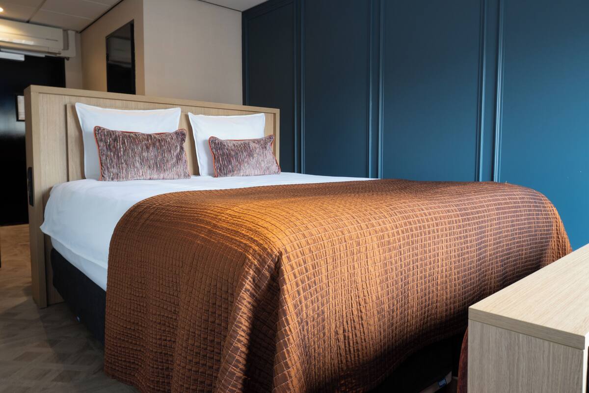 A hotel room with a bed, a wooden headboard, a blue accent wall, and a wooden nightstand.