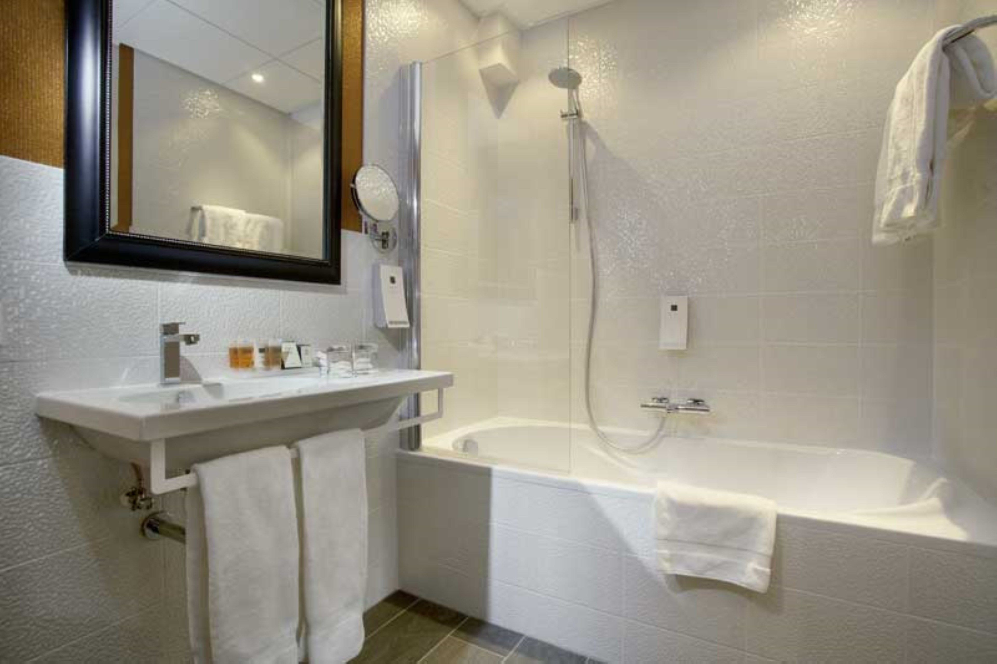 A modern bathroom with a white sink, mirror, and bathtub.