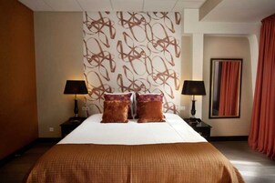 Une chambre d'hôtel avec un grand lit, deux lampes de chevet, un mur décoré d'un motif et un tableau encadré accroché au mur.