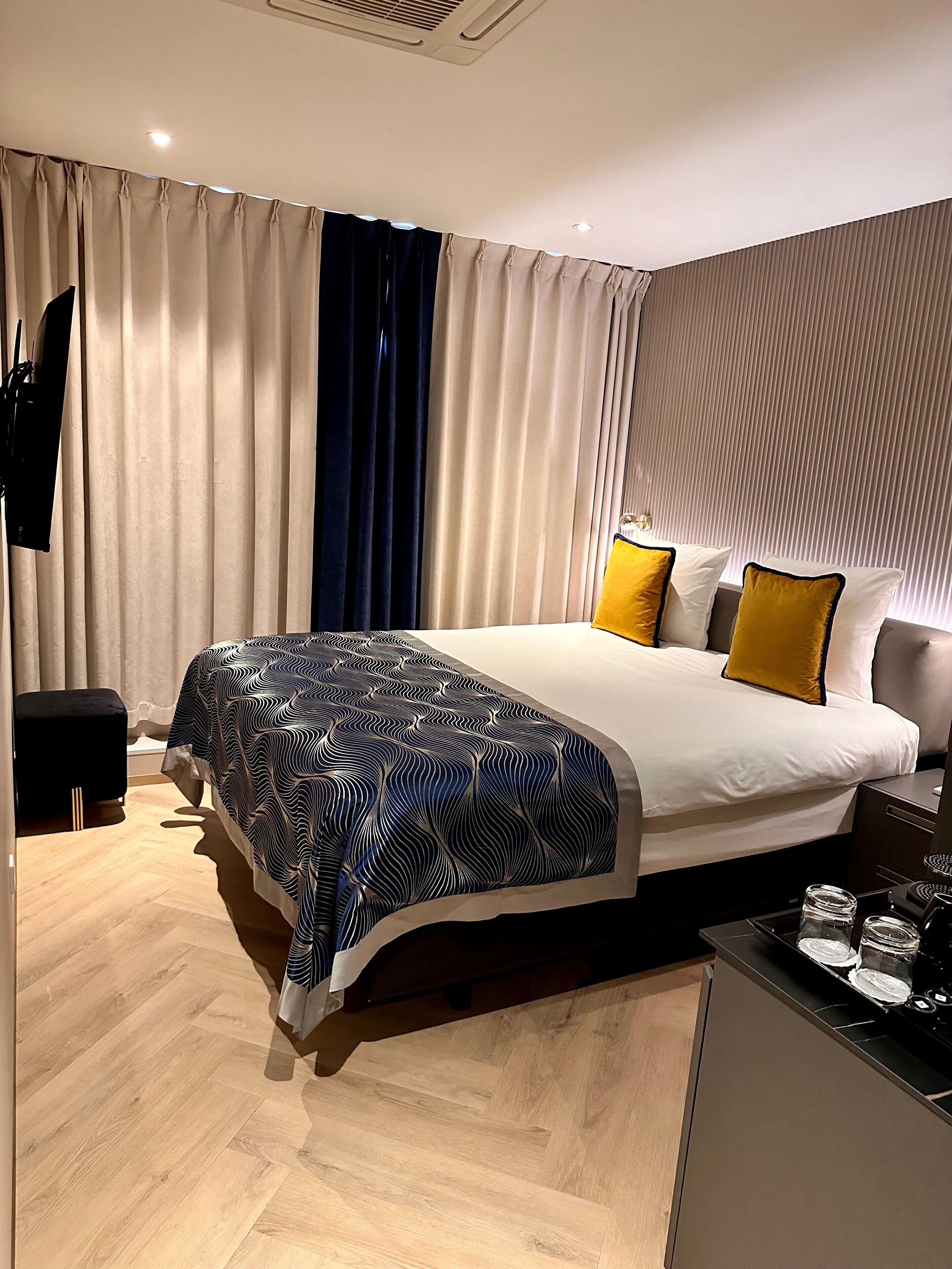 Quarto de hotel moderno com uma cama grande, uma mesa de cabeceira, uma escrivaninha pequena e um guarda-roupa.