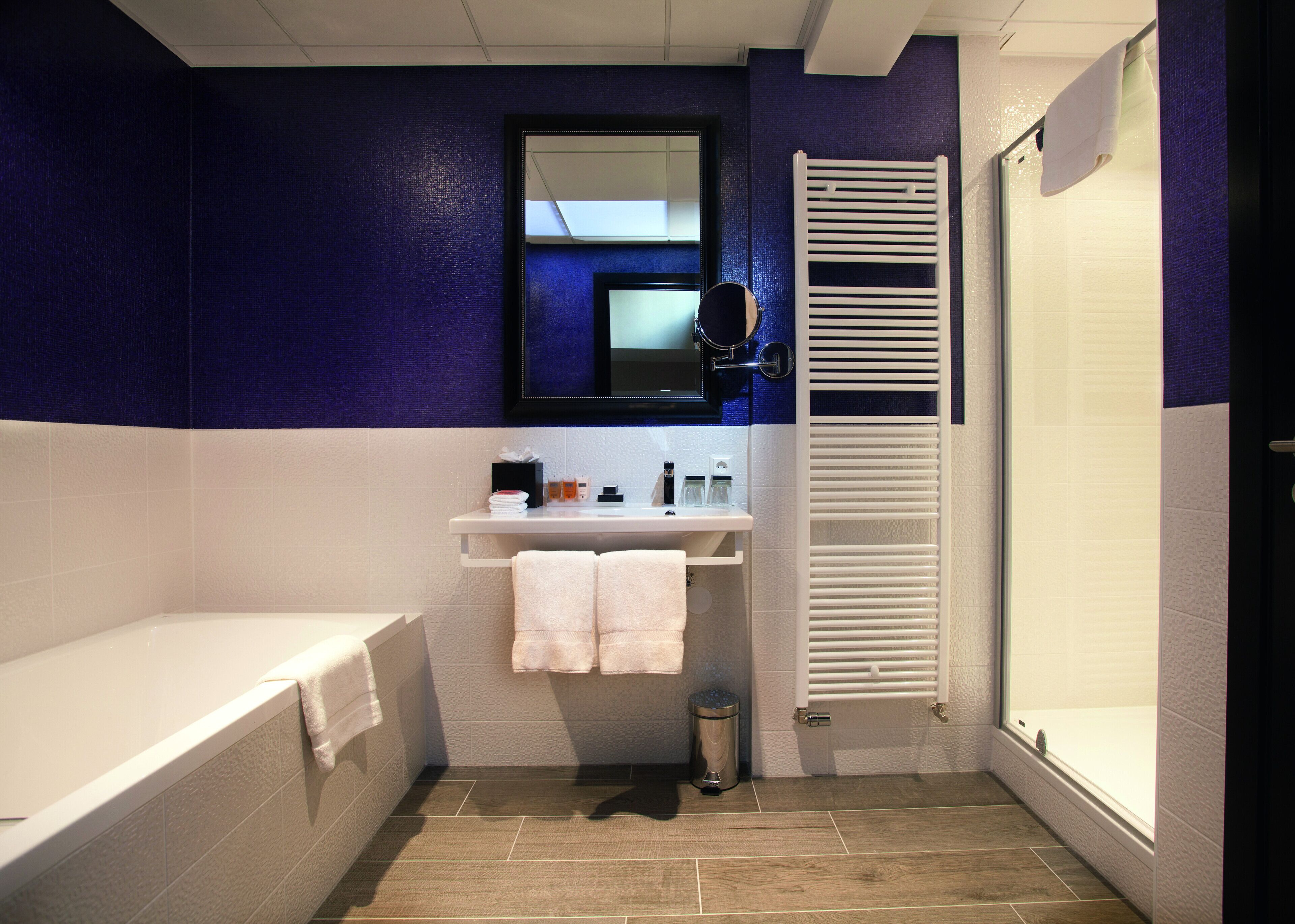 A bathroom with a bathtub, a sink with toiletries, a mirror, and a towel rack.