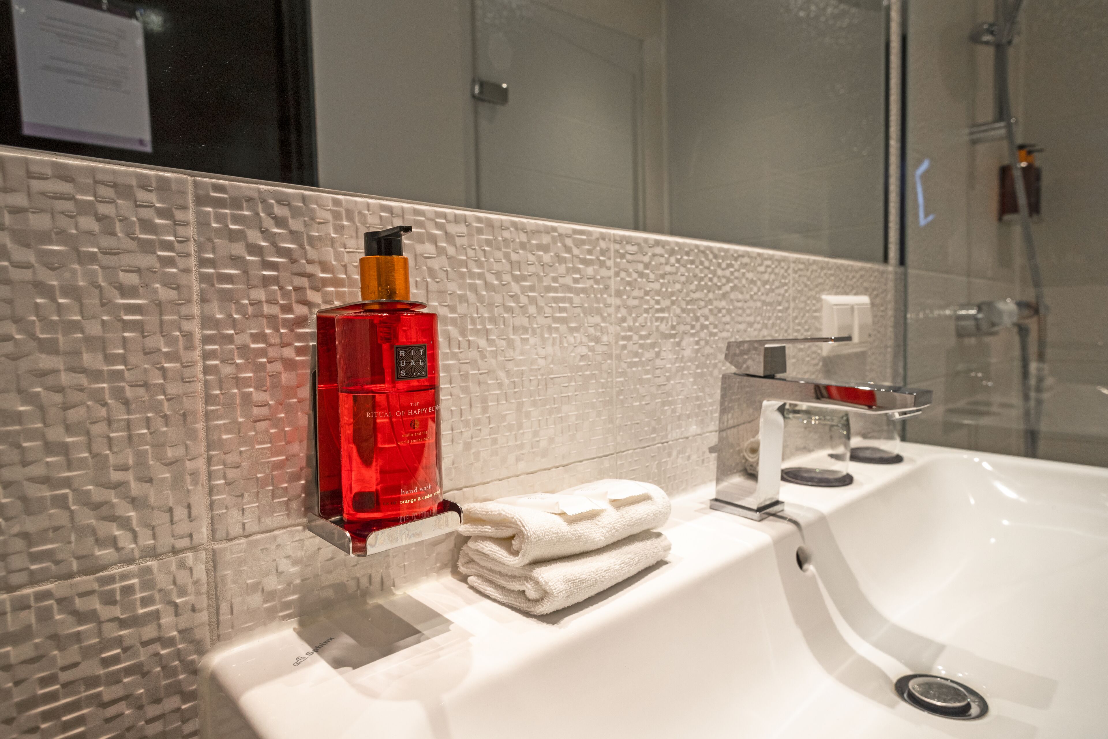 Ein Badezimmer mit strukturierter Wand, einem weißen Waschbecken, einer roten Flasche und einem gefalteten weißen Handtuch.