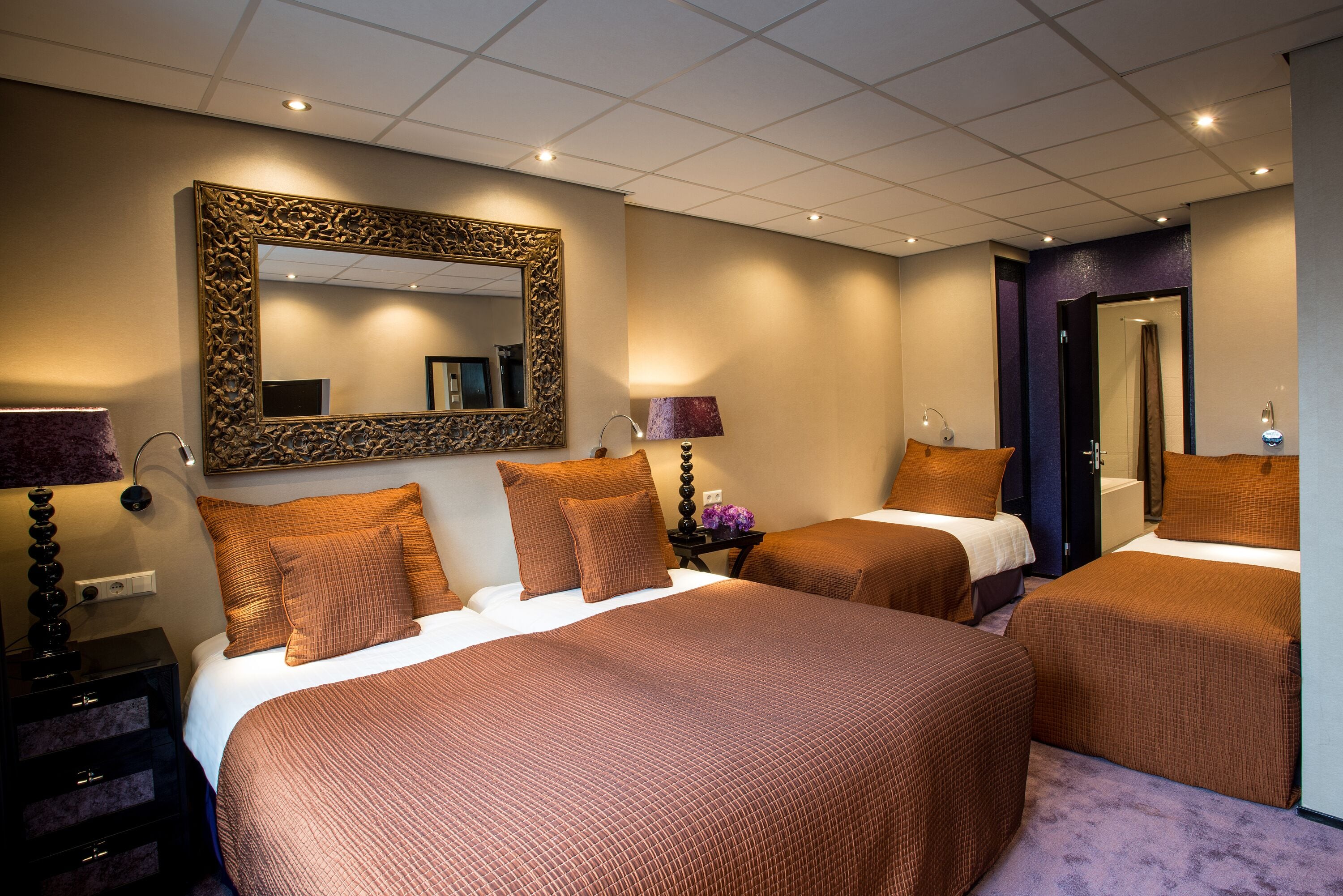 A hotel room with two beds, a large mirror, and a nightstand with a lamp.