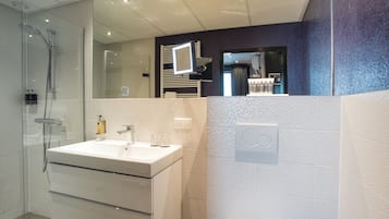 Uma casa de banho moderna com chuveiro envidraçado, lavatório branco e espelho.