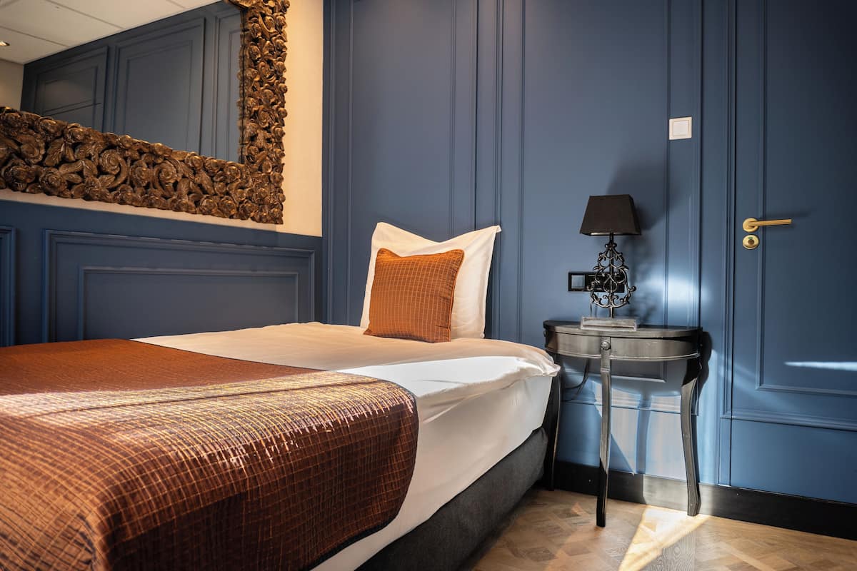 A hotel room with a bed, a nightstand, a lamp, and a door.