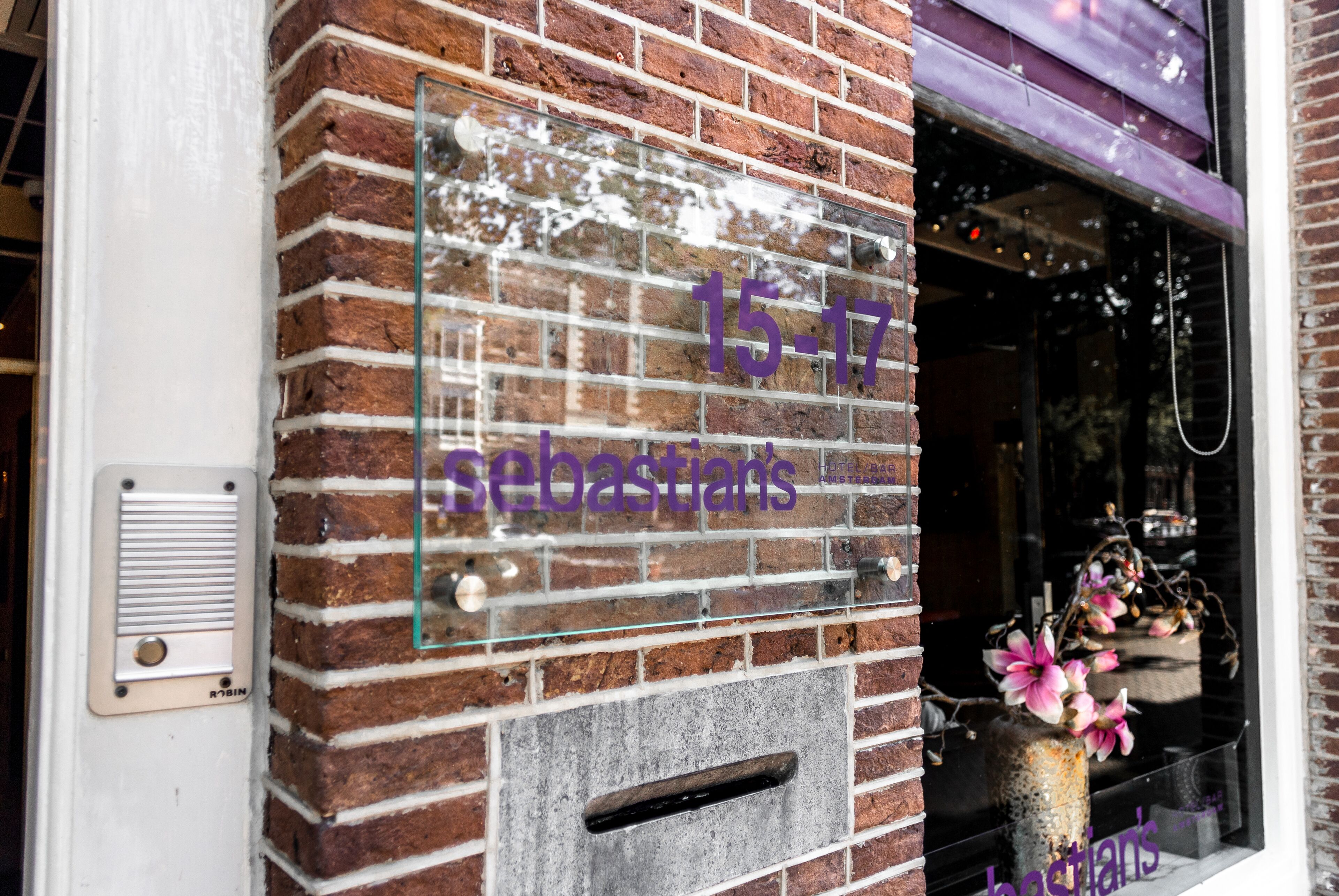 A brick wall with a window display featuring a sign reading "15-17 sebastians" and a decorative vase with flowers.